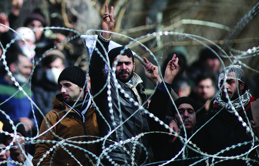 Migrants and refugees, wanted to cross into Greece are seen behind a wired fence. (Dimitri Tosidis/ Xinhua, 2020)